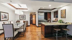 Una cocina moderna con una isla central, taburetes de bar, un comedor con una mesa larga y sillas, y un refrigerador a la vista.