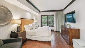 Un dormitorio con cama, mesita de noche, cómoda, televisor y ventana con vistas.