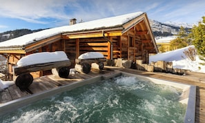 Uma cabana de madeira com banheira de hidromassagem e paisagem coberta de neve.