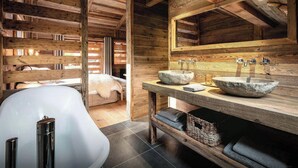 Une salle de bain rustique avec des poutres en bois, un grand lavabo en pierre et une baignoire blanche.