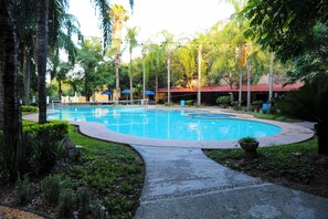 A swimming pool with a curved edge, surrounded by lush greenery and palm trees. - Campestre La Fuente  (Monterrey)