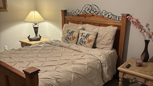 Un dormitorio con cama de madera, una mesita de noche con lámpara, un jarrón con flores y un ventilador de techo.