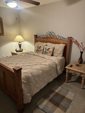 Un dormitorio con cama de madera, una mesita de noche con lámpara, un jarrón con flores y un ventilador de techo.