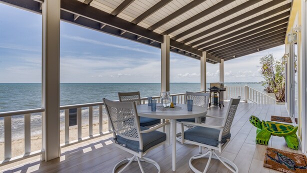 Uma área de estar coberta ao ar livre, com vista para o mar, que inclui uma mesa redonda com cadeiras, uma mesa pequena com um candeeiro e uma escultura decorativa de tartaruga.