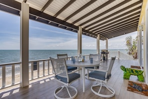 A covered outdoor seating area with a view of the sea, featuring a round table with chairs, a small table with a lantern, and a decorative turtle sculpture.