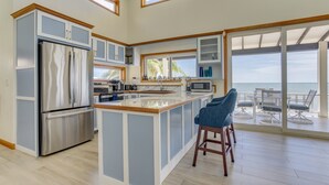 Cozinha moderna com ilha central, eletrodomésticos de aço inoxidável e vista para o oceano através de grandes portas deslizantes.