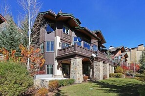 A multi-story building with a prominent balcony, stone pillars, and a well-maintained lawn. - Walk to Ski Lift | Après-Ski 4BR w/ Deck + Hot Tub (Vail)