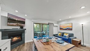 Una sala de estar moderna con chimenea, un comedor con mesa de madera dispuesta para dos personas y un sofá azul con cojines.