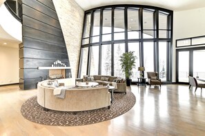A spacious living area with a large fireplace, a curved seating arrangement, and large windows offering a view of the outdoors. - KBM Resorts| Walk to Slopes, Sports Court, Private Home Theater, Sleeps 17, Outdoor Hot Tub PCO-184M (Park City)