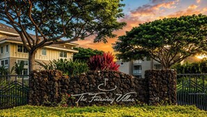 Un muro de piedra con el letrero 'The Fairway Villas', rodeado de setos y árboles bien cuidados.