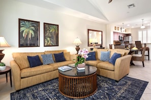 A living room with a sofa set, a coffee table, and a kitchen area in the background. - Fairway Villas Waikoloa | Golf Course View 2 BR | Free Car w/ 6+ Nts | FVW-L32 (Waikoloa Village)