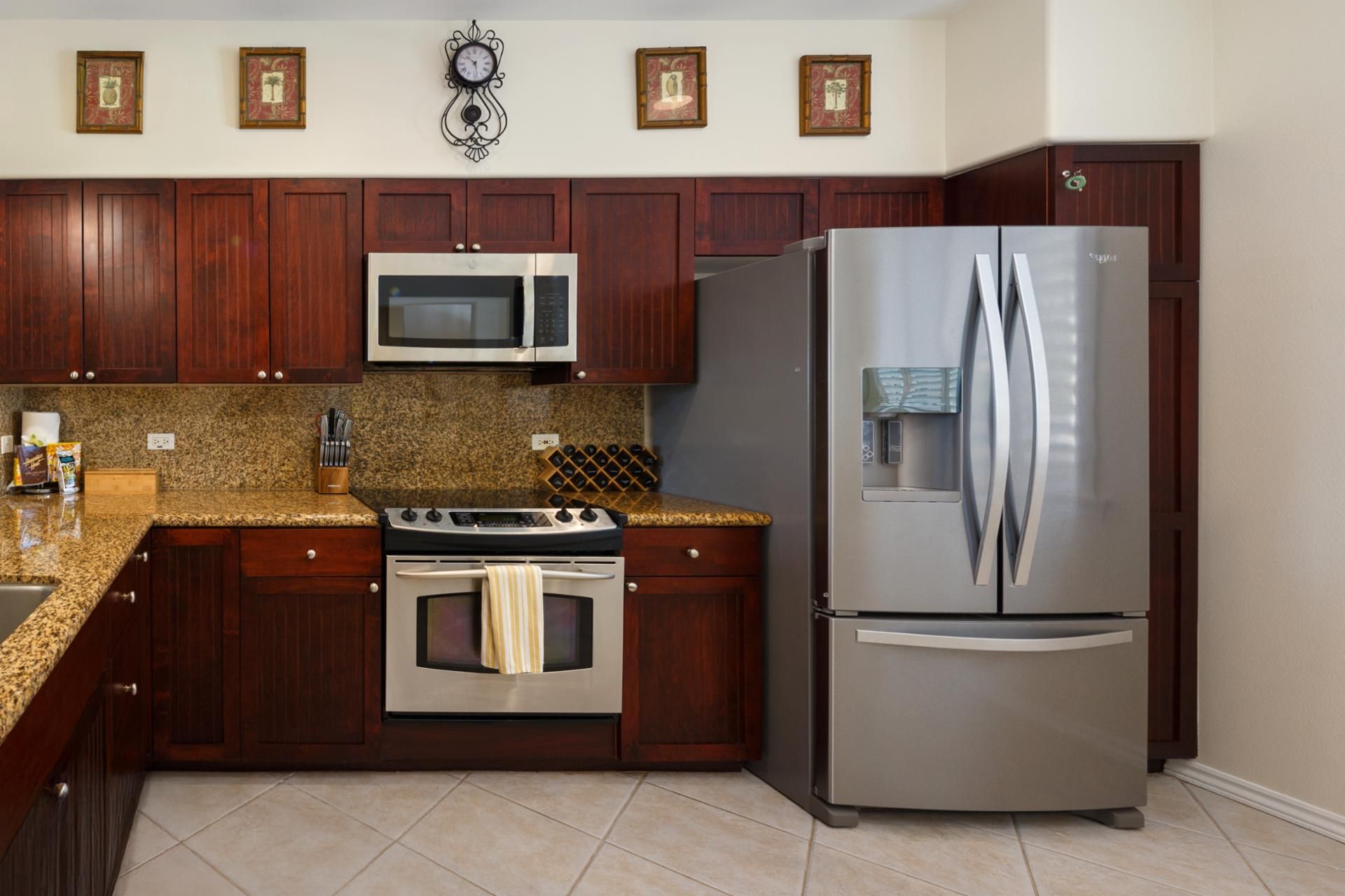 Una cocina con armarios de madera, electrodomésticos de acero inoxidable, encimeras de granito y un reloj en la pared.