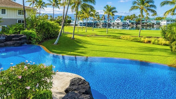 Una piscina con agua cristalina azul, rodeada de exuberante vegetación y palmeras.