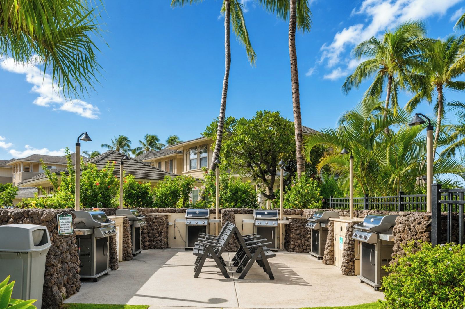A patio area with multiple barbecue grills, outdoor seating, and a stone wall.