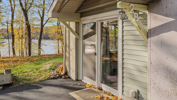 A building with a number '2B' on the door, a covered entrance, and a view of trees and a body of water. - Lake House—Unit B (East Lyme)
