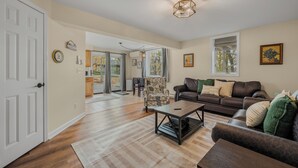 A spacious living room with a large window, a sofa, a coffee table, and a patterned armchair. - Lake House—Unit B (East Lyme)