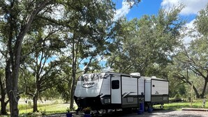 A Jayco RV parked in a campground with trees and gravel ground. - Cozy 1-bedroom mobile home in beautiful Spring Hill with AC (Spring Hill)