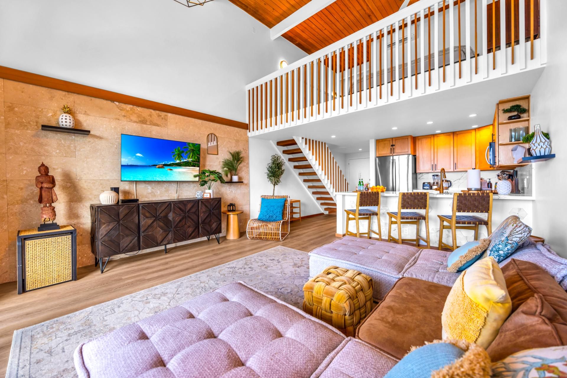 A spacious living area with a large flat-screen TV, a wooden staircase, a kitchen with modern appliances, and a cozy seating area with a plush sofa and ottoman.