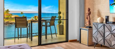 Quarto com uma grande porta de vidro deslizante que dá para uma varanda com vista para o oceano e paisagem tropical.