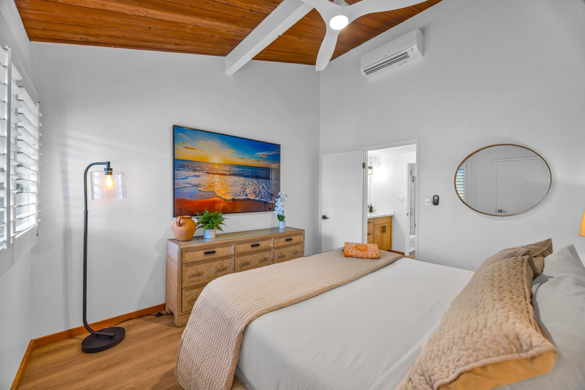 Une chambre à coucher avec un lit, une commode et un tableau représentant un coucher de soleil.