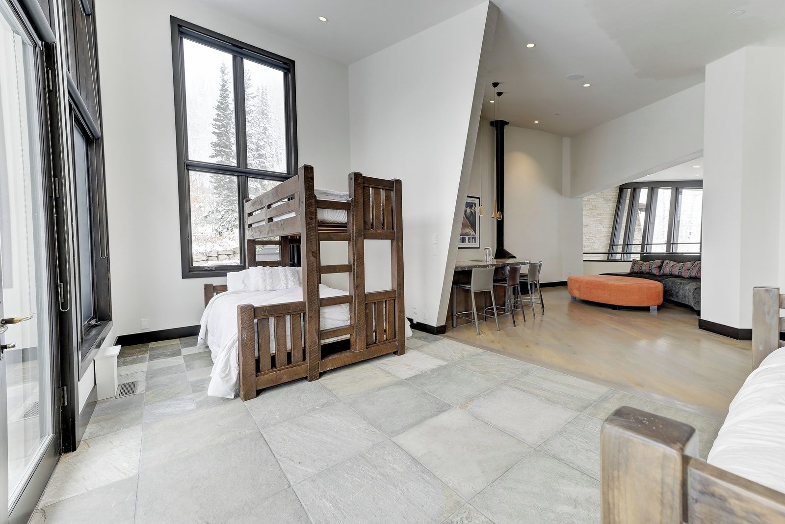 Un dormitorio moderno con literas, una zona de comedor con mesa y sillas, y un ventanal con vistas a árboles.