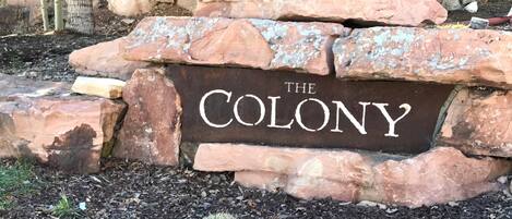 Een stenen bord met de tekst 'THE COLONY', omringd door stenen en houtsnippers.
