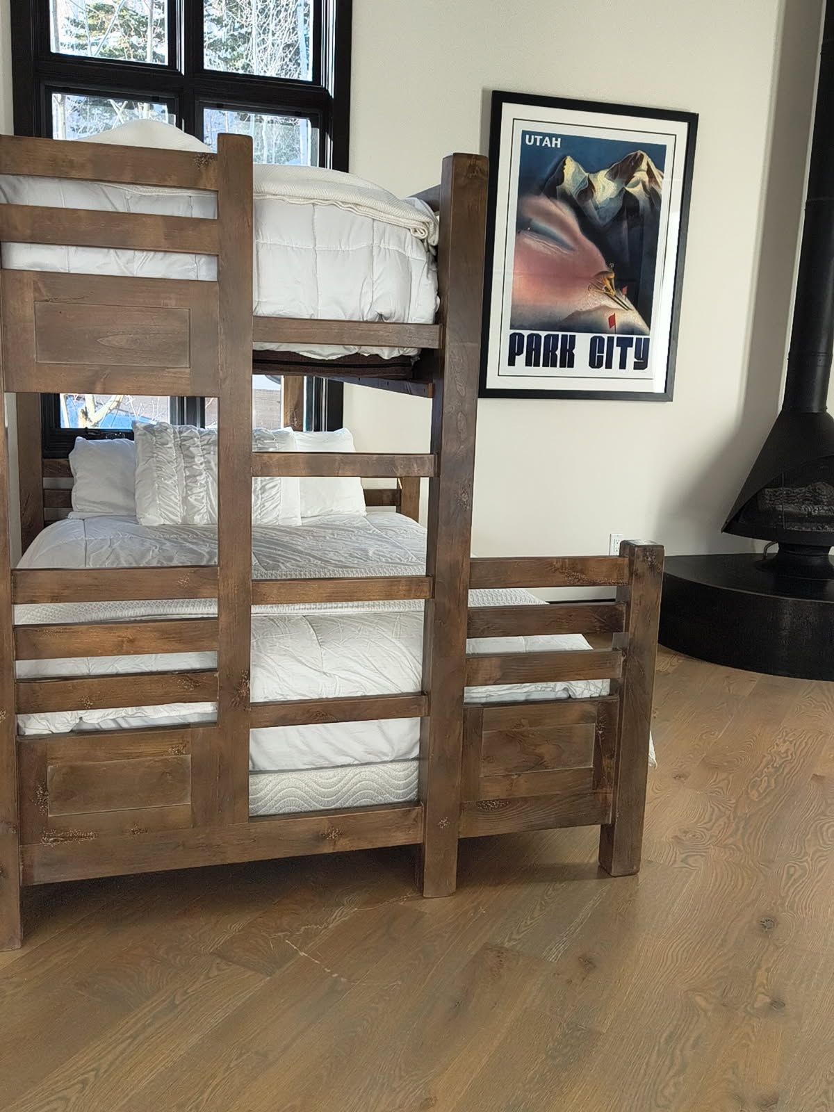 Een stapelbed met houten frame, een ingelijst poster aan de muur, en een houtkachel.