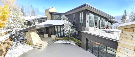 Een modern, meerlaags huis met een overdekte oprit, grote ramen en uitzicht op besneeuwde bomen.