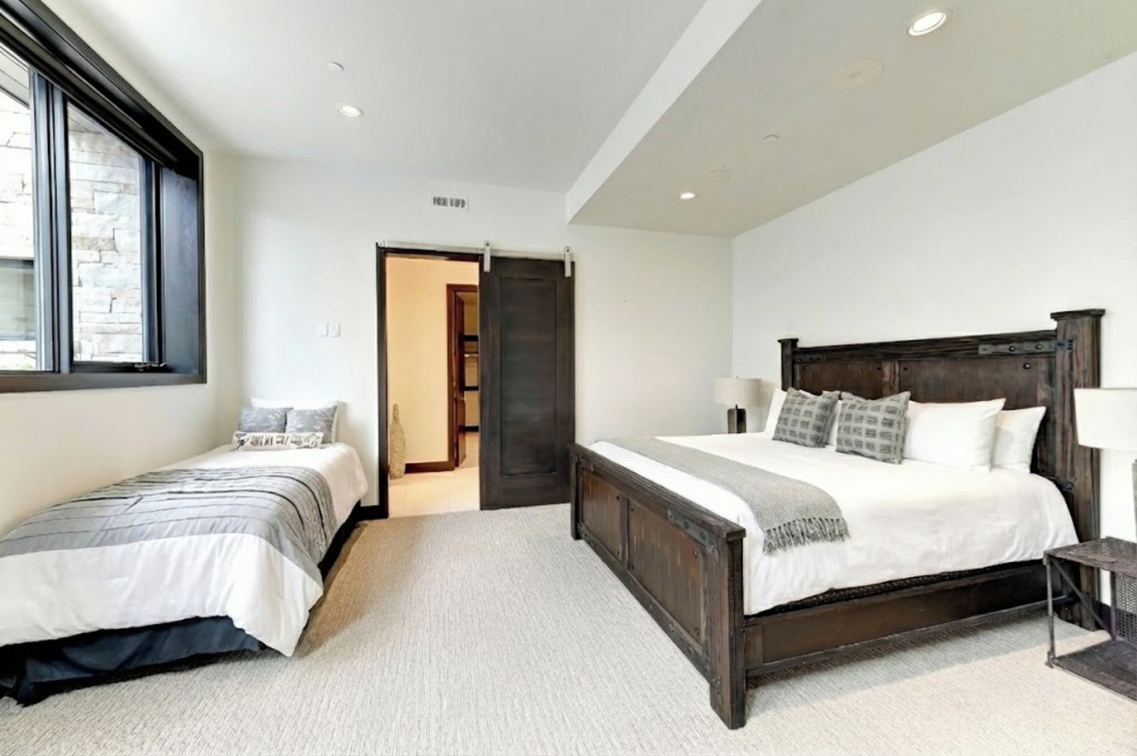 Un dormitorio con dos camas, cabecera de madera oscura, alfombra blanca y pared de piedra.