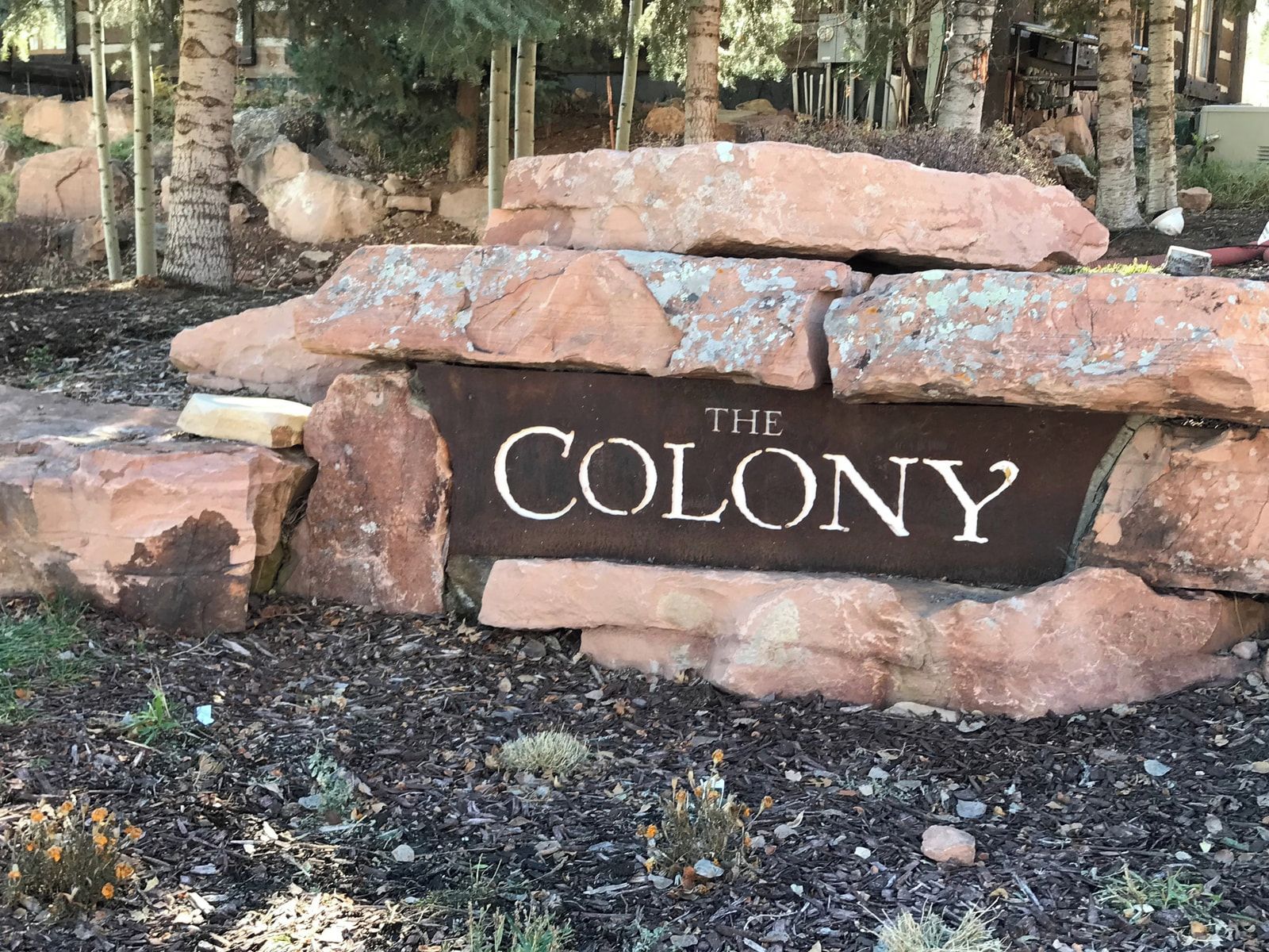 A stone sign with 'THE COLONY' written on it, surrounded by rocks and mulch.