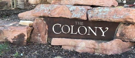 Ein Steinschild mit der Aufschrift 'THE COLONY', umgeben von Steinen und Mulch.