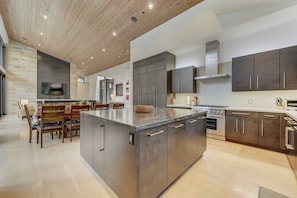 A modern kitchen with a central island, dark cabinetry, and a large TV mounted on the wall. - The Colony | Walk To Slopes, Hot Tub, Parking | KBM Resorts | Walk to Slopes, Hot Tub, Parking | 2 homes, 9 Bedrooms |  ML-2510 (Park City)