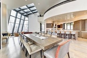 A modern kitchen with a curved island, a dining area with a long table, and large windows. - The Colony | Walk To Slopes, Hot Tub, Parking | KBM Resorts | Walk to Slopes, Hot Tub, Parking | 2 homes, 9 Bedrooms |  ML-2510 (Park City)