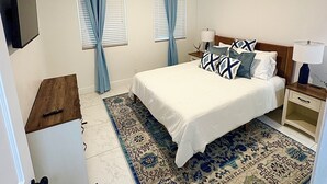 Ein Schlafzimmer mit Bett, Nachttisch, Lampe, Vorhängen und Deckenventilator.