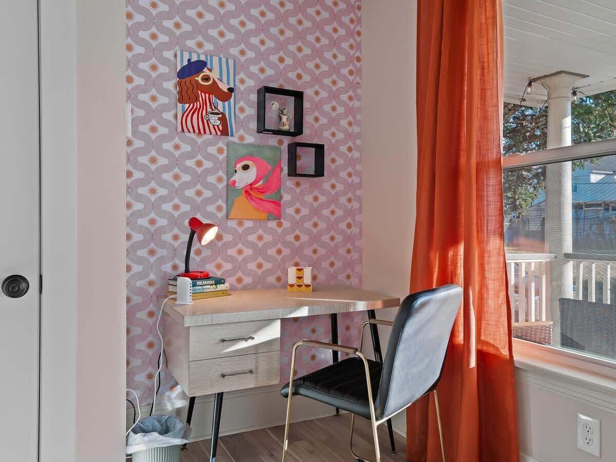 Una habitación con escritorio, silla y ventana con cortinas naranjas.