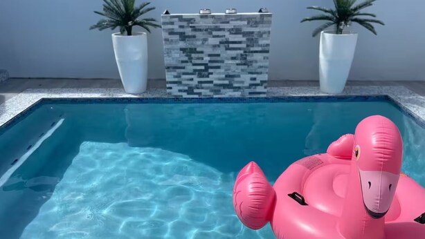 A swimming pool with clear blue water, a pink flamingo float, and two potted plants on the poolside.