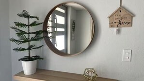 A round mirror on a wall, a small potted plant, a geometric decorative item, and a wooden sign with text.