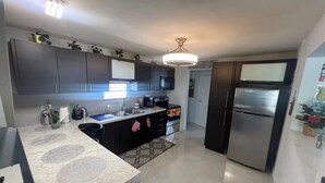 A modern kitchen with dark cabinets, a marble countertop, a built-in oven, and a stainless steel refrigerator.