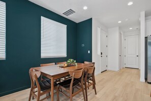A dining area with a wooden table and chairs, white blinds on the windows, and a white door in the background. - The Roost, Luxe Star Idaho Stay w/ 65" TV & Zippy Wi-Fi, Sleeps 8 (Star)