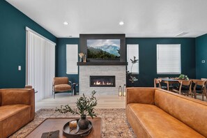 A modern living room with a fireplace, leather sofas, a dining area, and a large TV mounted above the fireplace.