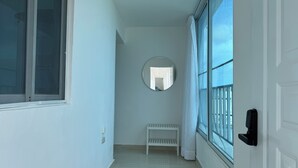 Ein schmaler Flur mit einer weißen Bank, einem runden Spiegel an der Wand und einer Tür mit schwarzem Griff.