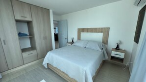 Ein Schlafzimmer mit einem Bett, Nachttischen, einem Kleiderschrank und einer Tür zu einem anderen Raum.