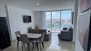 Ein modernes Wohnzimmer mit Essbereich, einem Flachbildfernseher und Blick auf die Stadt durch große Fenster.
