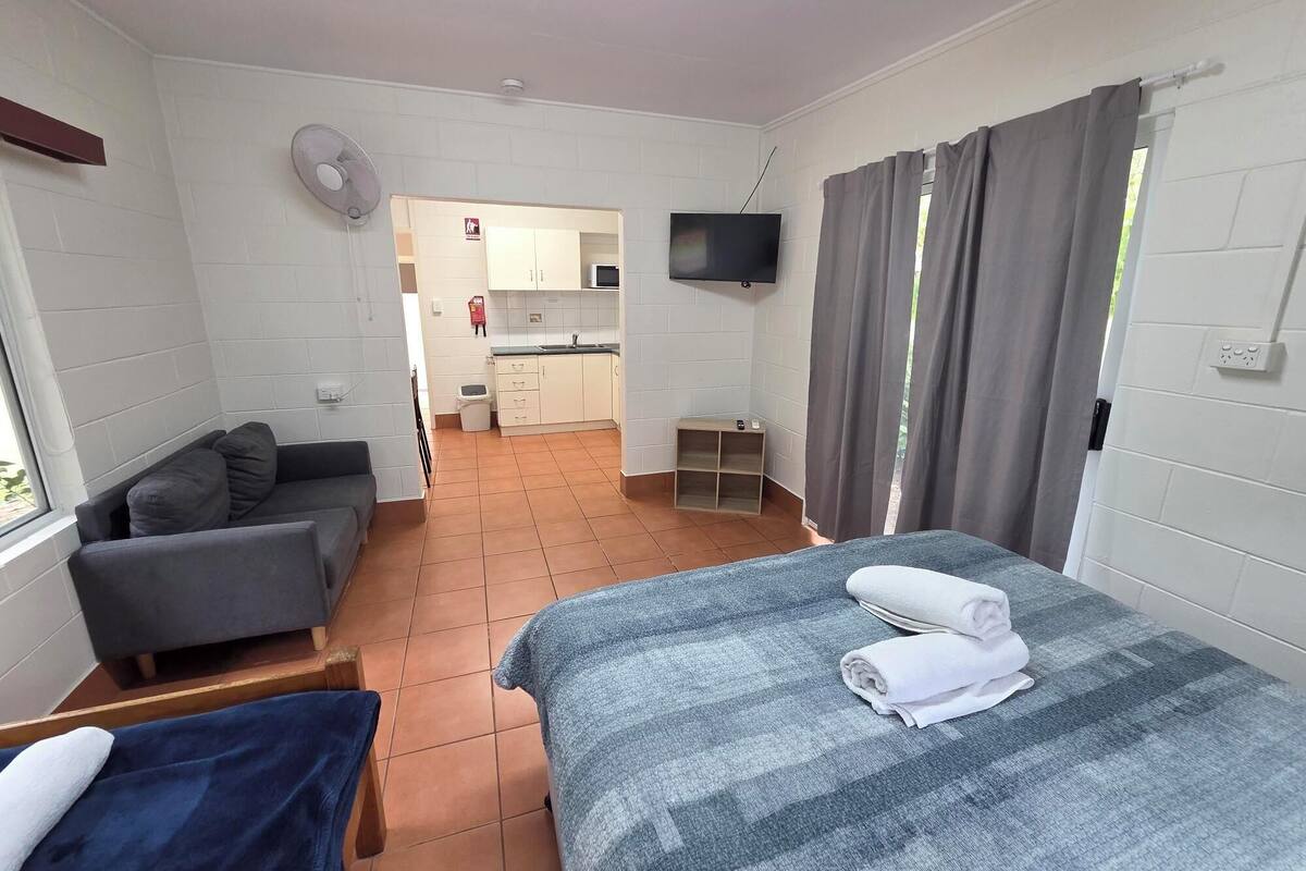 Habitación de hotel con cama, sofá, televisor, pequeña cocina y baño.