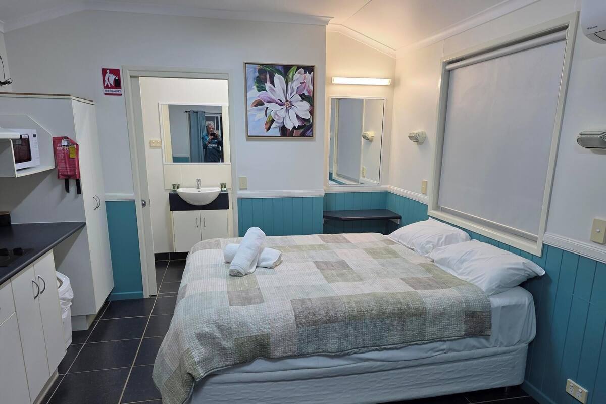 Habitación de hotel con cama, lavamanos, espejo y letrero indicando la manta ignífuga.