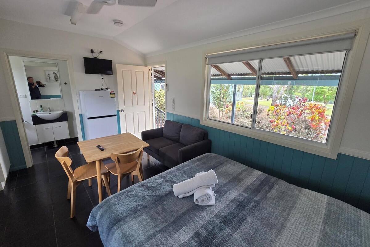 Una habitación con cama, escritorio, silla, sofá, televisor y ventana con vistas a zonas verdes.