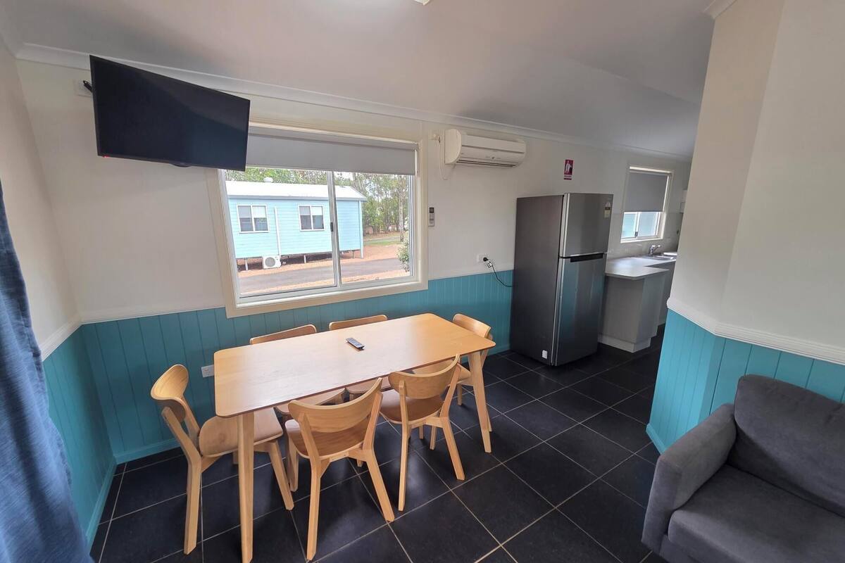 Cocina compacta con comedor, refrigerador y ventana con vista a una casa azul.