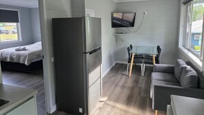 Pieni huone, jossa on sänky, jääkaappi, ruokapöytä tuoleineen, sohva ja seinälle asennettu televisio.