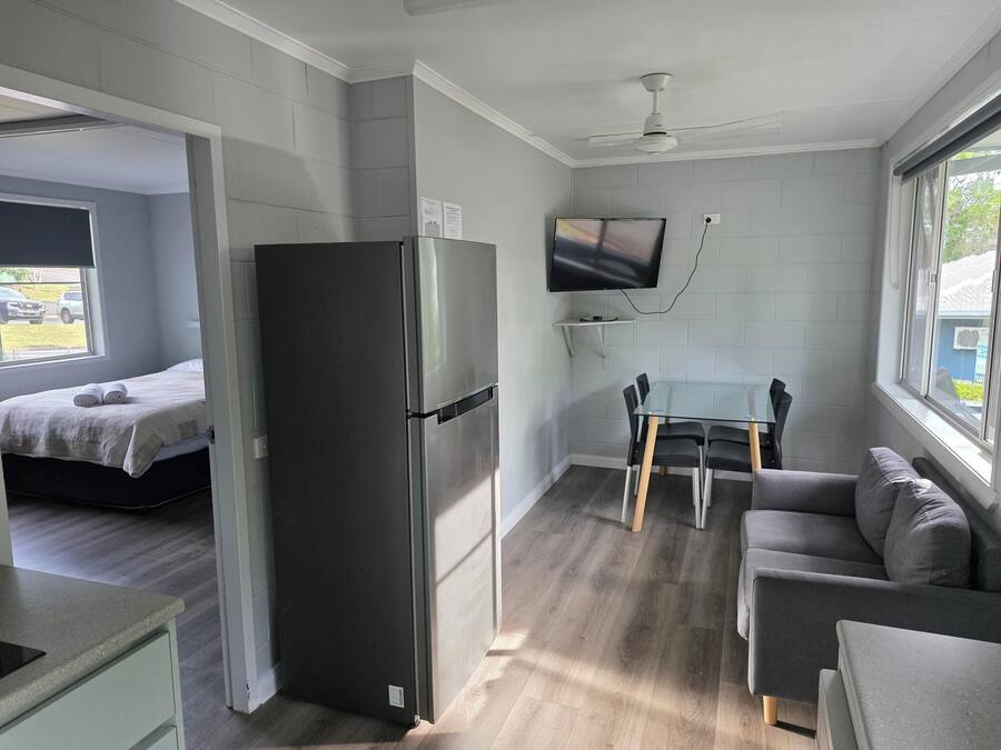 Une pièce de taille modeste comprenant un lit, un réfrigérateur, une table à manger avec des chaises, un canapé et un téléviseur fixé au mur.