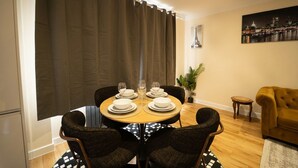 Comedor con una mesa redonda dispuesta para cuatro personas, rodeada de sillas de mimbre, un sofá y una mesita auxiliar.